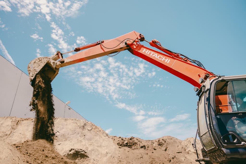 Excavator emptying a bucket of dirt onto the stockpile