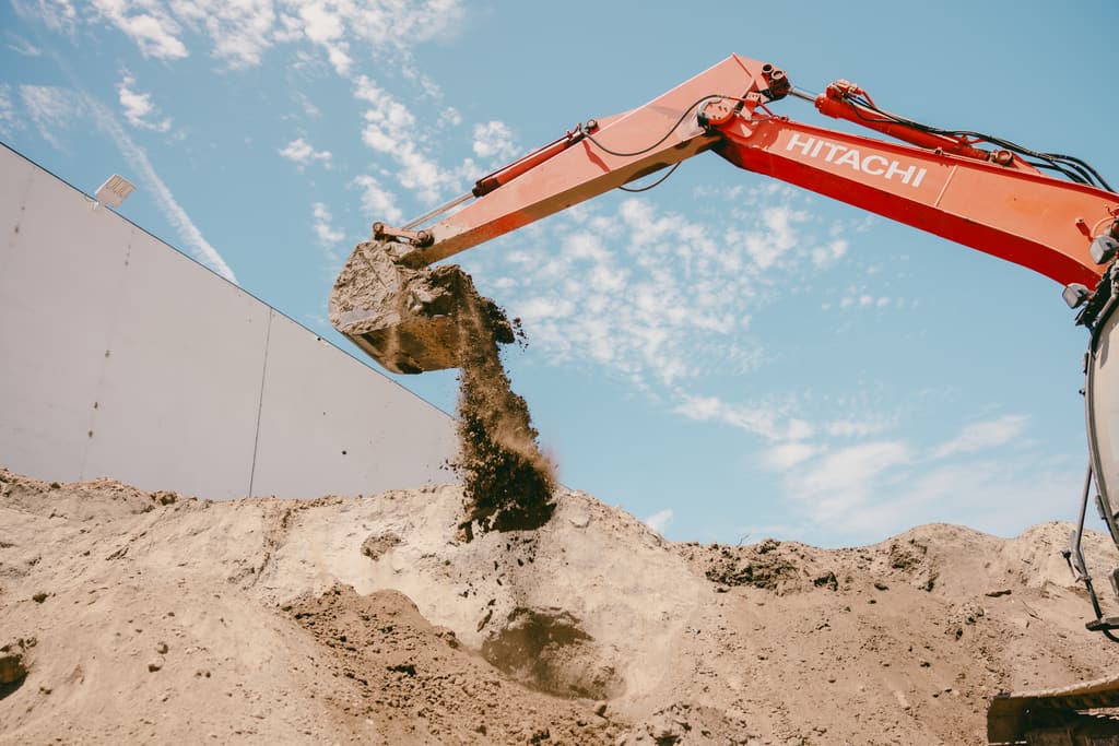Excavator arm raised high, dirt falling from the bucket against a clear sky