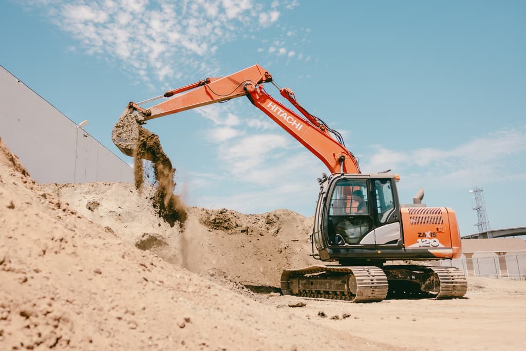 Excavator tipping dirt out of the bucket onto the pile