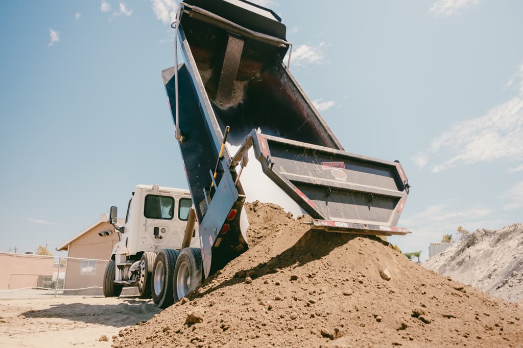 Dump truck with its bed fully raised unloading dirt at the yard