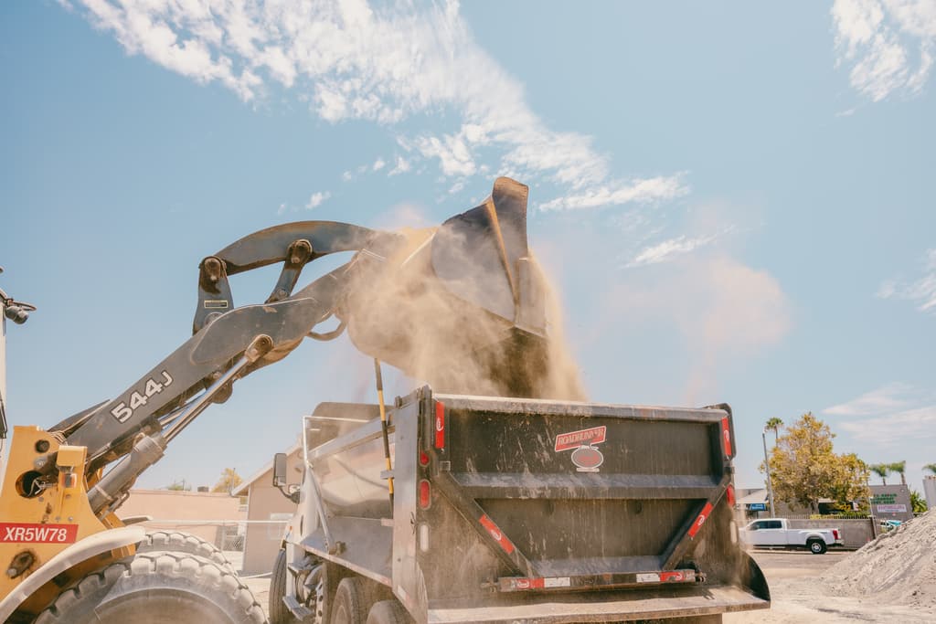 Wheel loader dumping a bucket of dirt into a haul truck at the yard